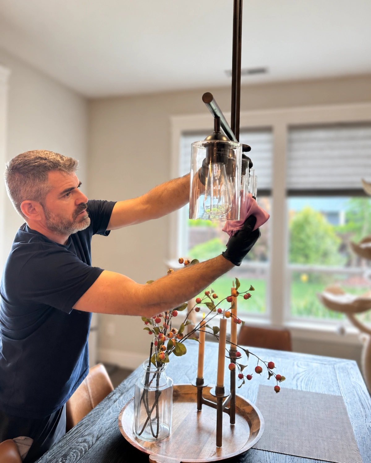 Clary Clean professional carefully wiping a glass light fixture above a dining table