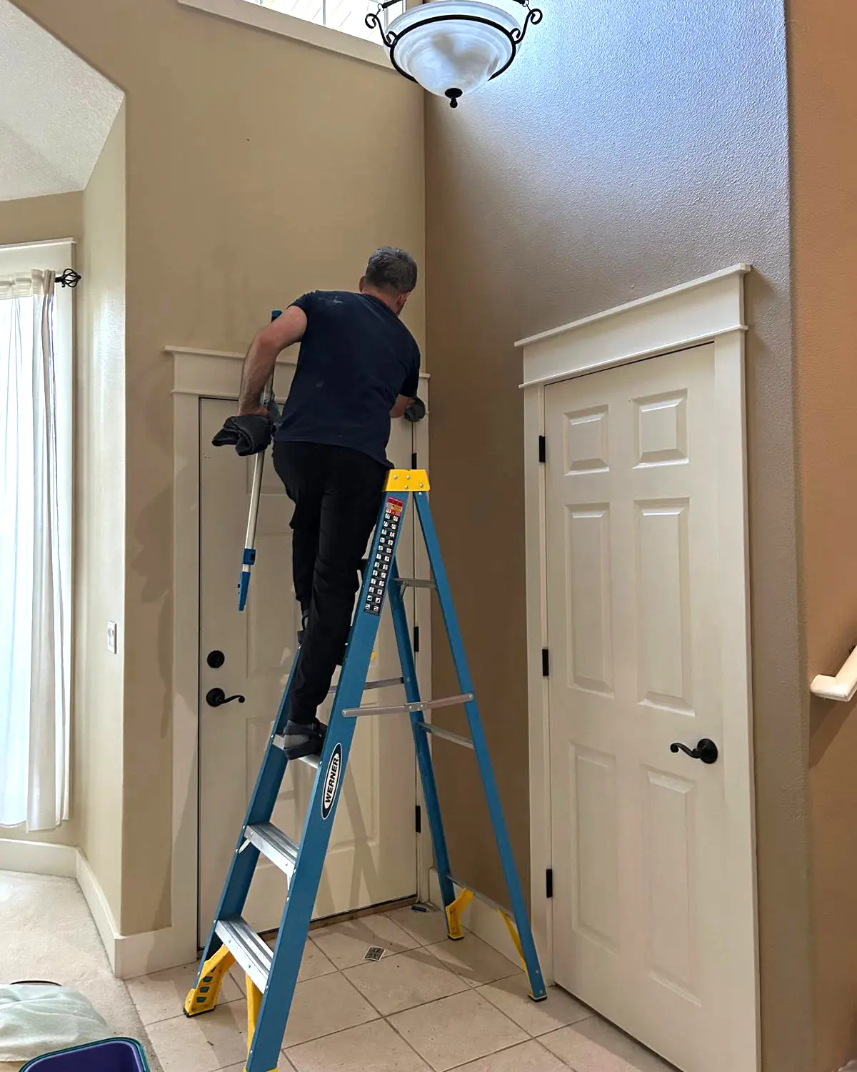 Daniel from Clary Clean high dusting and detail cleaning an entry area from a ladder during a residential cleaning visit