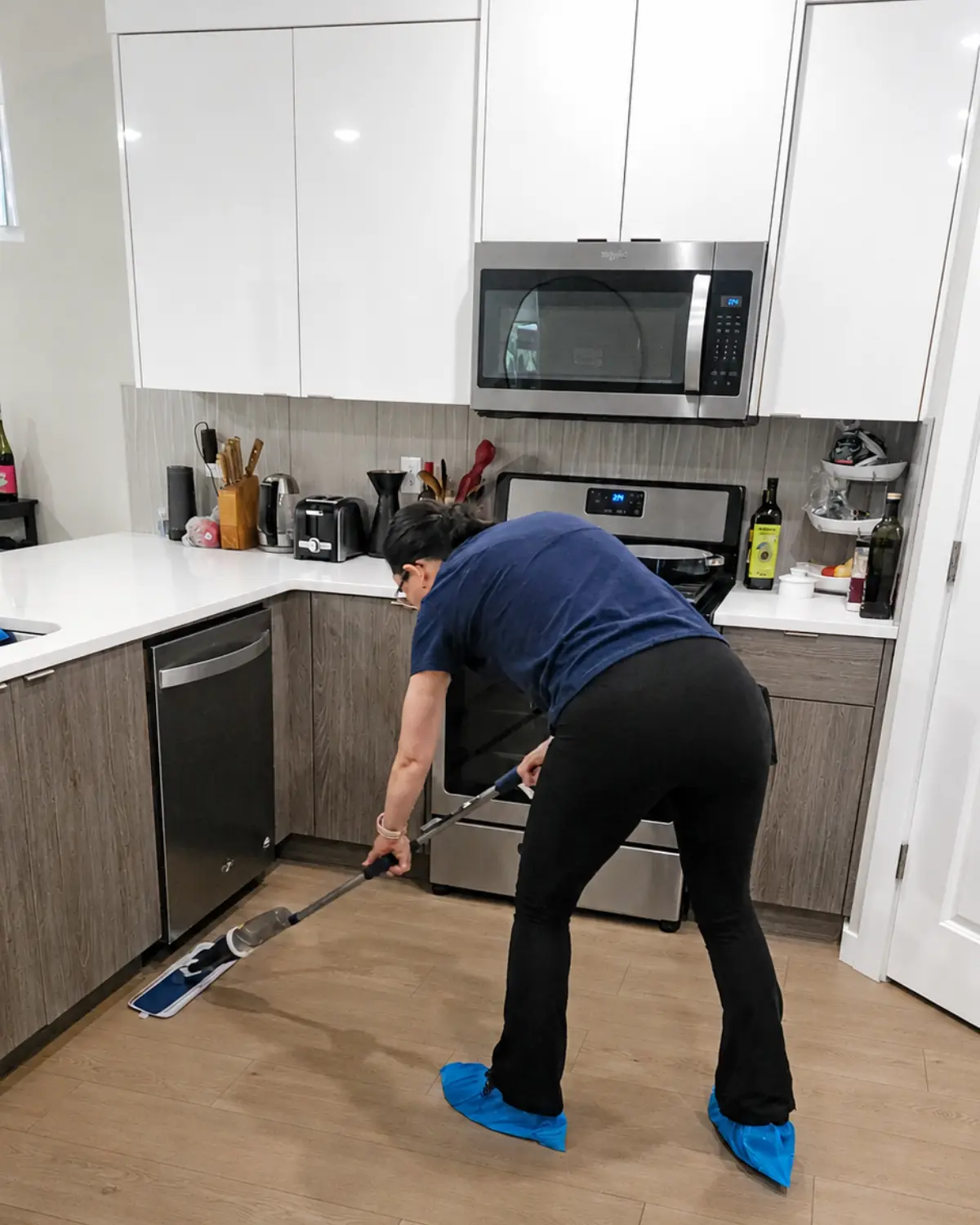 Cleaning professional mopping a kitchen floor around cabinets and appliances during a house cleaning visit