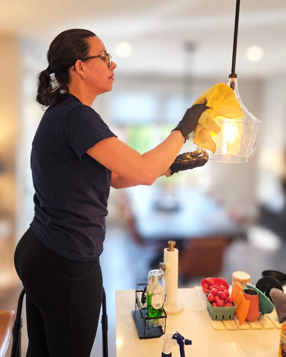 Clary Clean professional hand-cleaning a glass kitchen pendant light with a microfiber cloth