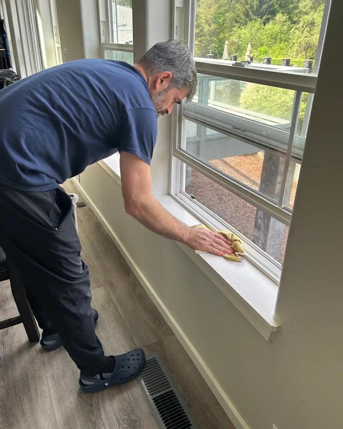 Cleaning professional wiping an interior window sill during a residential cleaning visit
