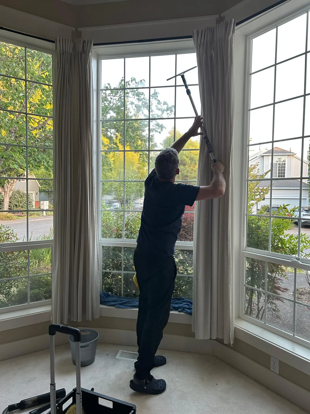 Clary Clean team member cleaning tall interior living room windows during a move-out cleaning service